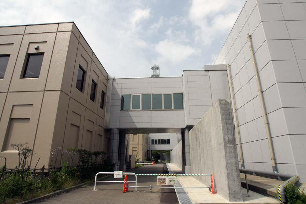 免震重要棟と事務所（左）とは、収縮する通路でつながっている。3.11以降に作られたコンクリートの石垣は、建物への放射線を遮蔽するためのもの。これだけでも相当の遮蔽効果があるという