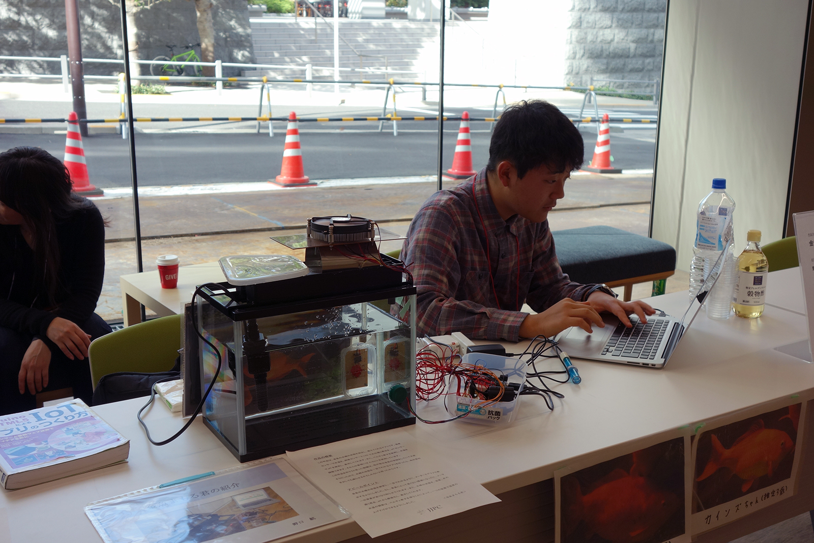 「金魚まもる君」を調整する野口航さん。水の濁り具合を検出するために、あらかじめ照度センサーとLEDを使うと決め、実際に透明な水や濁った水を入れてみてデータを蓄積。蓄積したデータから水の濁り具合を判断するプログラムを作成したという