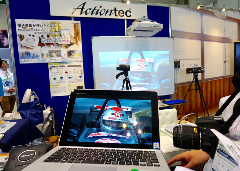 Actiontec ElectronicsブースではMiracastアダプター「<a href="https://www.screenbeam.com/ja/solutions/education-solutions/">ScreenBeam</a>」を展示（写真左）。ScreenBeam 960AはMacOSに対応しており、iOS対応に向けて準備中だという。 パソコンに表示された動画もディレイを感じることなく映写できる（写真右）