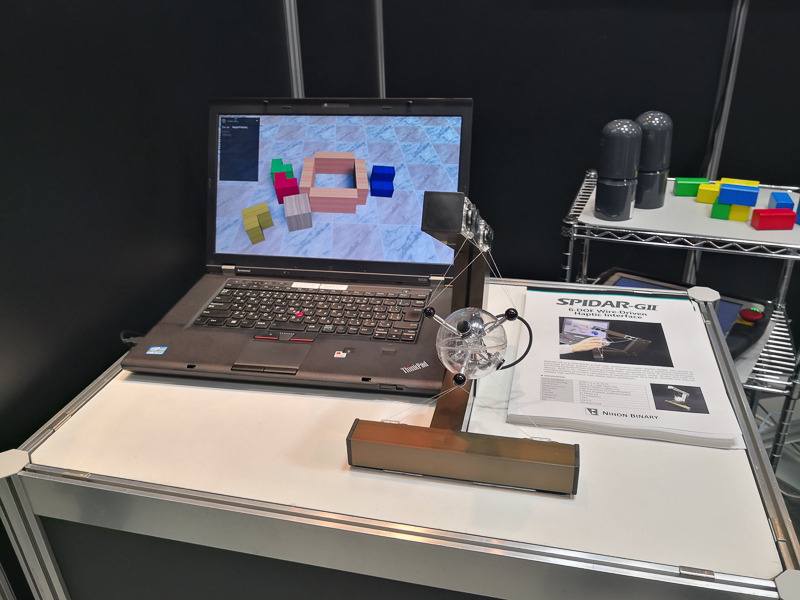 日本バイナリーのブースで体験できる「6軸力覚フィードバック装置」（左）と、ワイヤー式の6軸ハプティックデバイス「SPIDAR-GII」