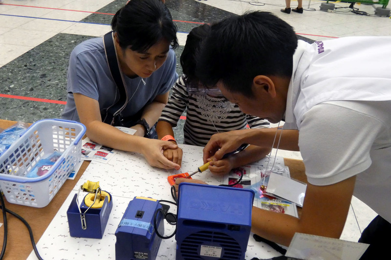 マクニカがアトリウムの特設会場で行っていた「Learn to Solder ～ハンダづけ体験コーナー～」。Maker Faireのマスコットキャラクター 「Makeyくん」のLEDバッジを作る