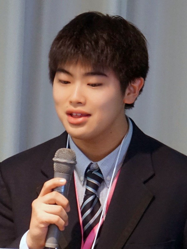 齋藤 尊さん（高2）。サッカーワールドカップ優勝チームに勝てるロボットチームを作ることは可能か。齋藤さんはそんな夢を目指していて、機械学習のひとつである強化学習を用いたロボットサッカーシミュレーションを発表した。バーチャルロボットに強化学習を行い、最終的にはその学習モデルを用いたロボットの実装に挑戦する。今回はバーチャルロボットが“サッカーをする”という動きの実現をめざした。強化学習したAgentの学習モデルを、実装予定ロボット「Plen2」のバーチャルロボットに移行する時に苦労したと述べた