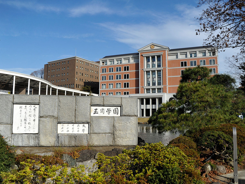 首都圏郊外の広大な敷地に幼稚園から大学院までが揃った玉川学園キャンパス内、校舎の他に植物工場など多くの施設がある。正門とすぐそばに見えるのは大学の施設