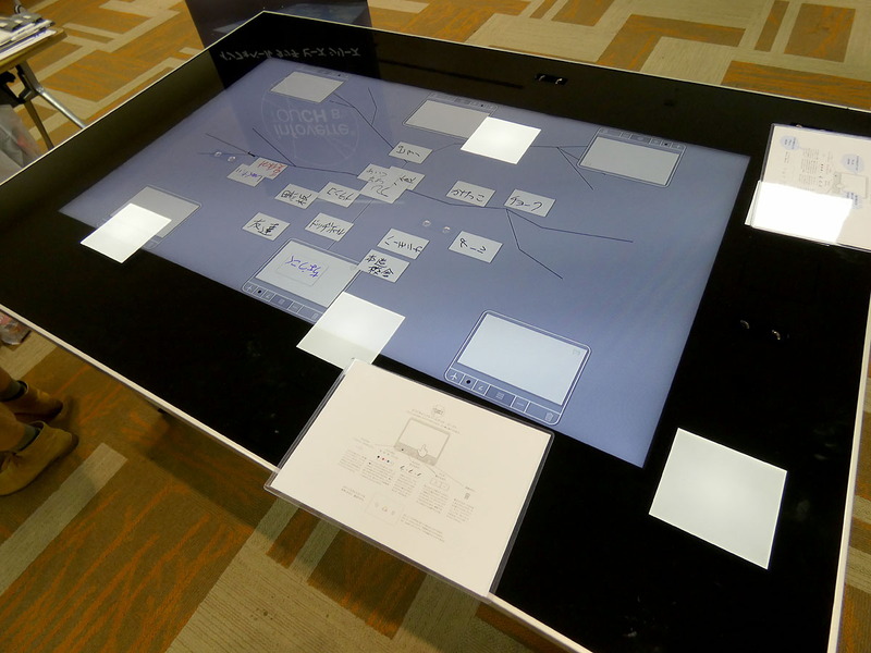 チームのディスカッションをガイドするデジタルテーブル「infoverre TOUCH B’s」(AGC株式会社)。自分のアイデアを指でデジタルカードに入力し、カードをグルーピングして集約できる。マンダラモード、マインドマップモードなど議論の展開に合わせて活用できる