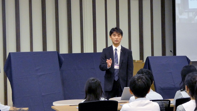 鈴木教諭の背後に意味深に並ぶ布に覆われた3つのオブジェ