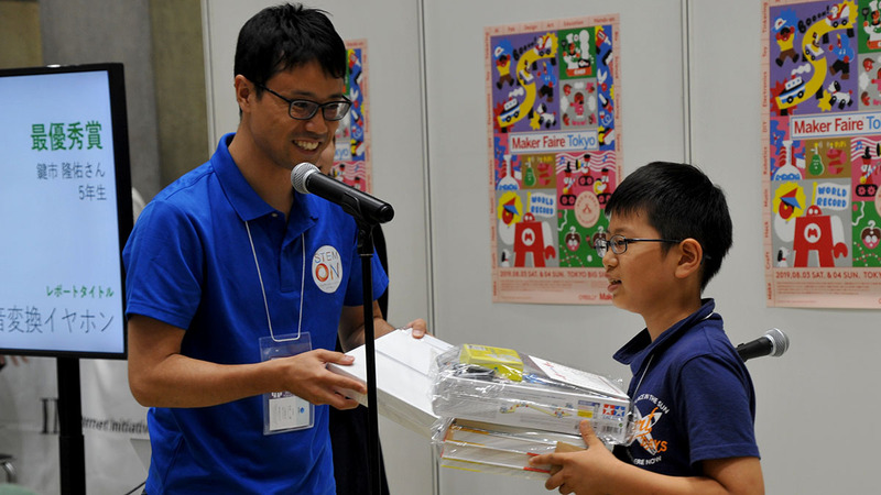 最優秀賞に選ばれたアイデアレポートとたくさんの商品を受け取る受賞者