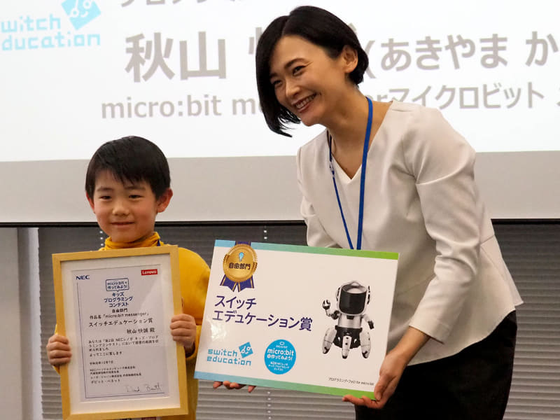 自由部門のスイッチエデュケーション賞に選ばれた秋山快誠さんには、審査員の株式会社スイッチエデュケーション 代表取締役社長 小室真紀氏からプログラミング・フォロ for micro:bitが贈られた