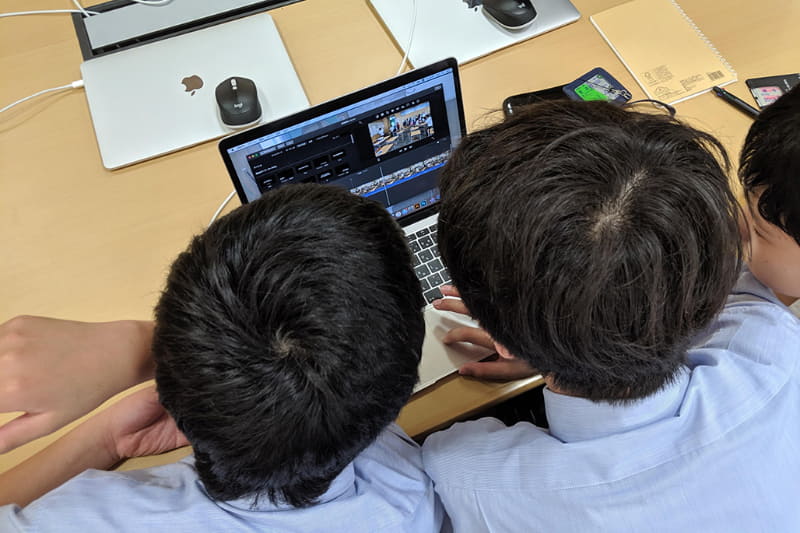 MacBookやiPadを囲んで作業する生徒たち、どうしてものぞき込むような不自然な姿勢になり見づらさがある