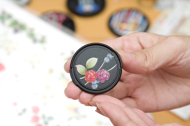 実際に取り出してくれた転写シールを貼ったレンズキャップ。シール自体はきれいなのだが、土台となるキャップ自体が黒地なので、輪郭がぼやけてしまっている。これではいくらきれいなシールを貼ったとしても、色やデザインが映えないだろう。