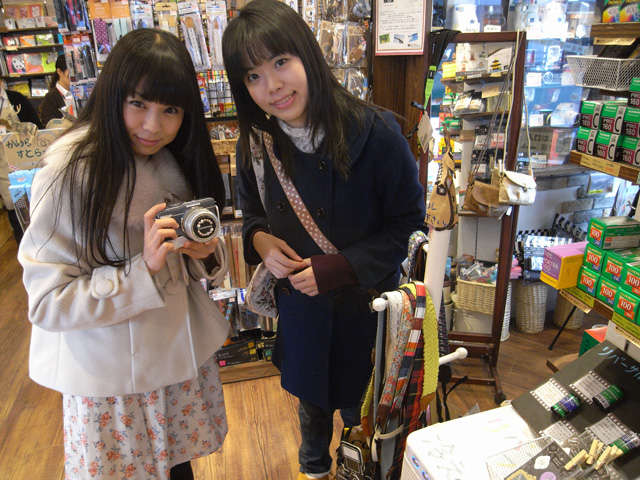 今回は、池袋のカメラ専門店「BIC PHOTO」で、高宮葵さん（右）と葉月さくらさん（左）がショルダーストラップ選びに挑みます。さくらさんの自作デコレンズキャップにも注目